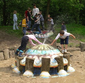 Qualle als Wasserspiel im Sandkasten und spielenden Kindern